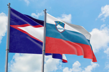 Slovenia and American Samoa flags waving in the wind against white cloudy blue sky together. Diplomacy concept, international relations.