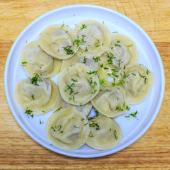 Traditional Russian hand-made dumplings with butter and herbs on a white plate.