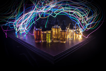 Smoke clouds and vape liquid bottles on dark background. Light effects. Useful as background or...