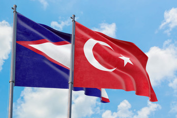 Turkey and American Samoa flags waving in the wind against white cloudy blue sky together....