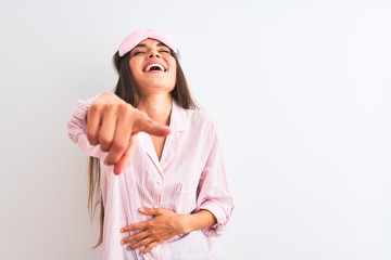 Young beautiful woman wearing sleep mask and pajama over isolated white background laughing at you, pointing finger to the camera with hand over body, shame expression