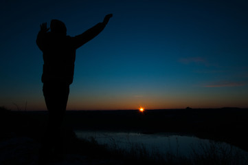 Silhouetted men on a background of blue sky and sunset. With arms raised. Prayer to God. Glorification.