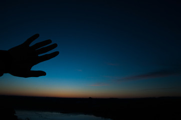 Silhouette of hands on a background of blue sky sunset. The rays of the sun through your fingers.