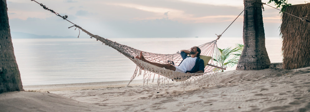 A man enjoys calm, lies in a hammock on the background of the ocean and sunset.