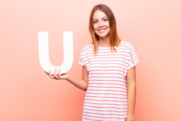 young pretty red head woman excited, happy, joyful, holding the letter U of the alphabet to form a...