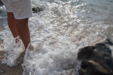 Male legs in the waves against the backdrop of a sunset on the beach