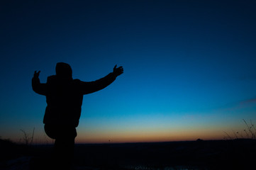 Fototapeta premium Silhouetted men on a background of blue sky and sunset. With arms raised. Prayer to God. Glorification.