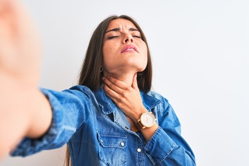 Beautiful woman wearing denim shirt make selfie by camera over isolated white background Touching painful neck, sore throat for flu, clod and infection