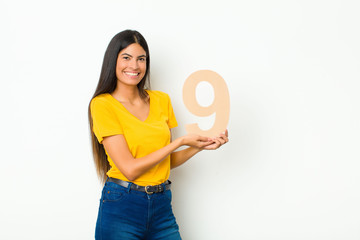 young latin pretty woman excited, happy, joyful, holding a number 9.