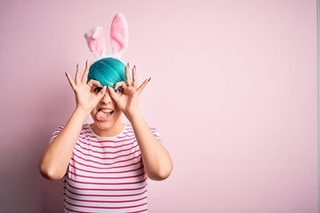 Young woman with fashion blue hair wearing easter rabbit ears over pink background doing ok gesture...