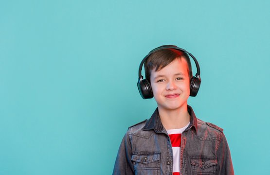 Kid Enjoying Music On His Headphones, Listening To Music. Handsome Young Stylish Kid In Headphones Standing Against Blue Background And Smiling