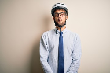 Young businessman wearing glasses and bike helmet standing over isolated white bakground making fish face with lips, crazy and comical gesture. Funny expression.