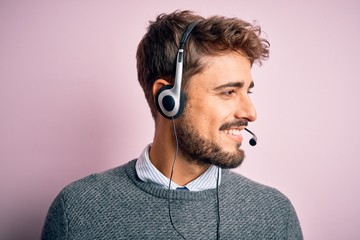 Young call center agent man with beard wearing headset over isolated pink background looking away...
