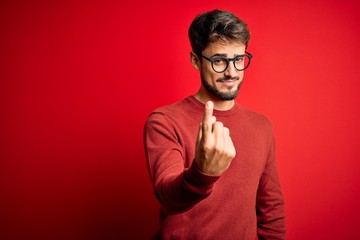 Young handsome man with beard wearing glasses and sweater standing over red background Beckoning come here gesture with hand inviting welcoming happy and smiling