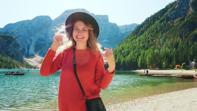 bright juicy colors, happy pretty girl in red sweater black hat on shore Lake Braies, cheerful lady spinning, smiling at camera. positive emotions tourist reserve Italy and Dolomites fly blond hair