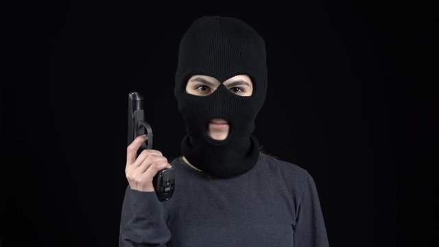 A woman in a balaclava mask is standing with flowers. The thug discards a bouquet of flowers and takes out a gun. On a black background.