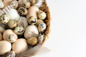 White and brown Easter eggs and feathers in a basket on white background. Natural healthy food and organic farming, easter and spring concept.