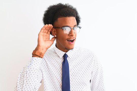 Young african american businessman wearing tie and glasses over isolated white background smiling with hand over ear listening an hearing to rumor or gossip. Deafness concept.