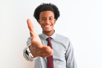 Young african american businessman wearing tie standing over isolated white background smiling friendly offering handshake as greeting and welcoming. Successful business. © Krakenimages.com