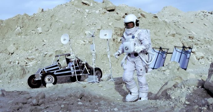 Caucasian woman cosmonaut in the full special armor gumping on the ground of the Moon crater at the moonwalker and radars. Outdoors.