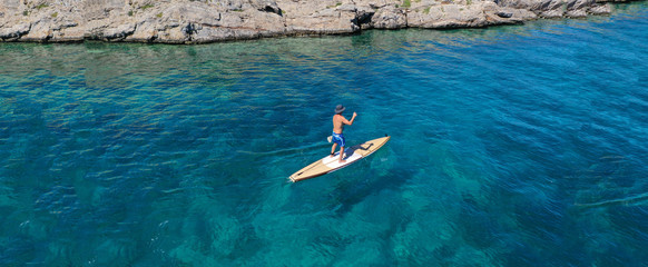 Aerial drone ultra wide top down photo of male Stand Up Paddle board surfer paddling in tropical...