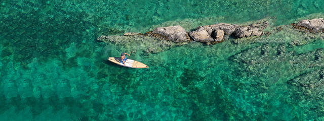 Aerial drone ultra wide top down photo of male Stand Up Paddle board surfer paddling in tropical...
