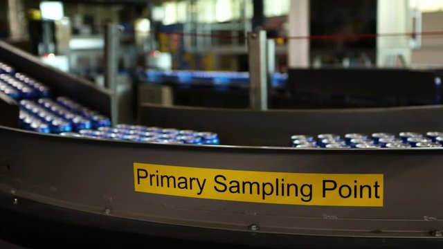 pan shot of Belt conveyor system with selective focus on yellow sign sticker of primary sample point, beer can boxes moving on lines in the background