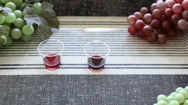 Close up shot of three small cups of different red wine varieties on the table next to grapes decoration, person's hand choosing a cup and drink it