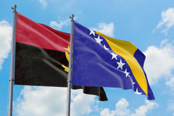 Bosnia Herzegovina and Angola flags waving in the wind against white cloudy blue sky together. Diplomacy concept, international relations.