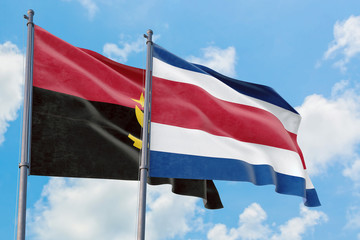 Costa Rica and Angola flags waving in the wind against white cloudy blue sky together. Diplomacy concept, international relations.