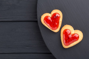 Naklejka na ściany i meble Heart shaped cookies decorated for Valentine's Day. Free space for text. Two heart shaped cookies with jam on a black wooden table. Like postcard 