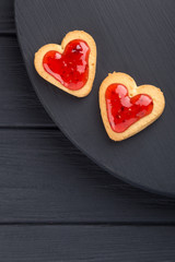 Obraz na płótnie Canvas Heart shaped cookies decorated for Valentine's Day. Free space for text. Two heart shaped cookies with jam on a black wooden table. Like postcard 