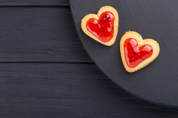 Fototapeta na wymiar Heart shaped cookies decorated for Valentine's Day. Free space for text. Two heart shaped cookies with jam on a black wooden table. Like postcard 