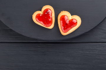 Heart shaped cookies decorated for Valentine's Day. Free space for text. Two heart shaped cookies with jam on a black wooden table. Like postcard 