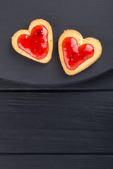 Obraz na płótnie Canvas Heart shaped cookies decorated for Valentine's Day. Free space for text. Two heart shaped cookies with jam on a black wooden table. Like postcard 