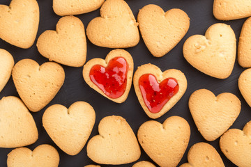 Heart shaped cookies decorated for Valentine's Day. Free space for text. Two heart shaped cookies with jam on a black wooden table. Like postcard 