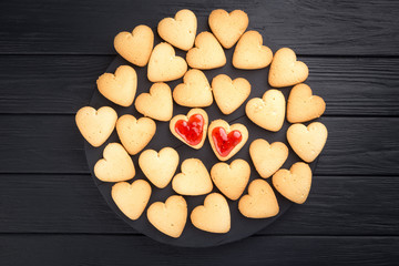 Heart shaped cookies decorated for Valentine's Day. Free space for text. Two heart shaped cookies with jam on a black wooden table. Like postcard 