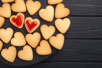 Heart shaped cookies decorated for Valentine's Day. Free space for text. Two heart shaped cookies with jam on a black wooden table. Like postcard 