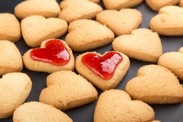 Heart shaped cookies decorated for Valentine's Day. Free space for text. Two heart shaped cookies with jam on a black wooden table. Like postcard 