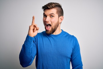 Fototapeta premium Young handsome blond man with beard and blue eyes wearing casual sweater pointing finger up with successful idea. Exited and happy. Number one.