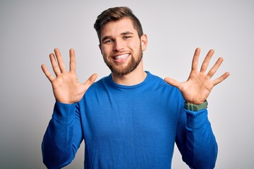 Young handsome blond man with beard and blue eyes wearing casual sweater showing and pointing up with fingers number ten while smiling confident and happy.