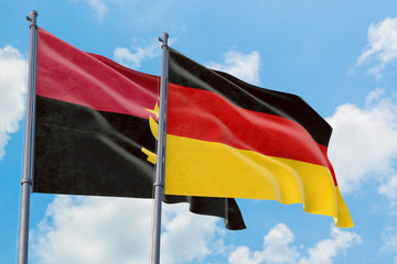 Germany and Angola flags waving in the wind against white cloudy blue sky together. Diplomacy concept, international relations.