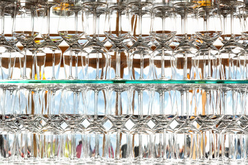 Wall of many empty transparent wine glasses on glass shelf at bar cafe or restaurant against backlit window. Abstract alcoholic beverages pub background. Close-up detail glassware pattern