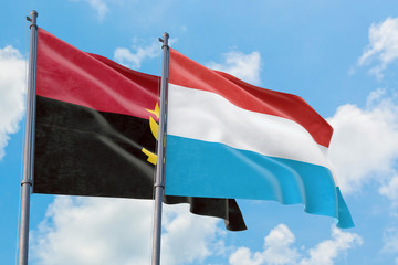 Luxembourg and Angola flags waving in the wind against white cloudy blue sky together. Diplomacy concept, international relations.