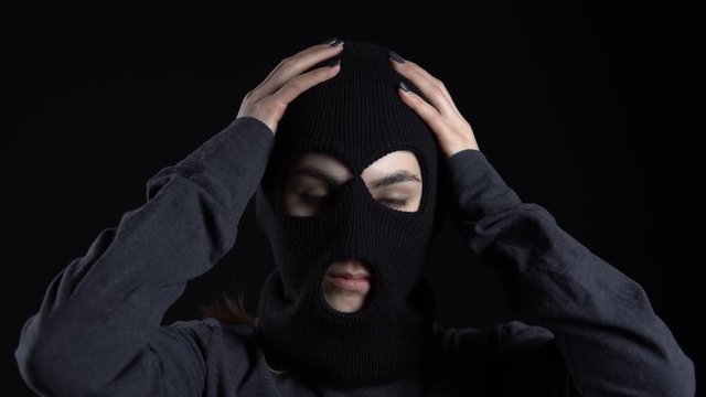 A young woman is putting on a balaclava mask. Bandit on a black background close-up.