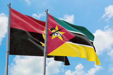 Mozambique and Angola flags waving in the wind against white cloudy blue sky together. Diplomacy...