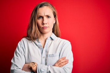 Young beautiful blonde woman wearing casual denim shirt over isolated red background skeptic and...