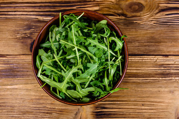 Ceramic bowl with arugula leaves on wooden table. Top view
