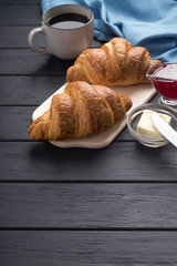 Fresh croissants on a black wooden table. Served with coffee, coffeepot, butter, jam, blue napkin. Fresh French Baked Croissants. Warm Fresh Buttery Rolls. Free space for text. 