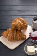 Fresh croissants on a black wooden table. Served with coffee, coffeepot, butter, jam, blue napkin. Fresh French Baked Croissants. Warm Fresh Buttery Rolls. Free space for text. 